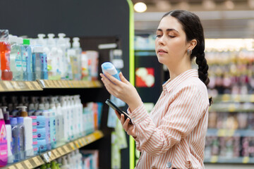Portrait of Caucasian young woman keeps shampoo bottle. Choice of care cosmetics in supermarket....