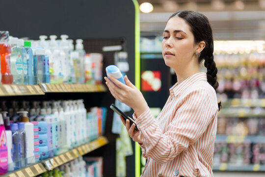 Portrait of Caucasian young woman keeps shampoo bottle. Choice of care cosmetics in supermarket. Concept of shopping and purchase