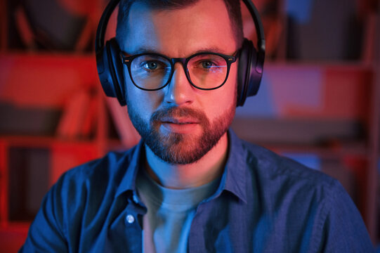 Portrait of man that is in headphones and glasses. Indoors, neon lighting