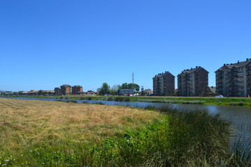 a river and some green areas near an urbanization of buildings and houses