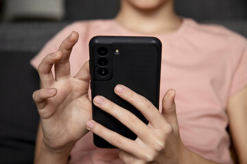 A teenage girl using a smartphone, presses her finger, reads social networks on the Internet, types text or plays video games, a mobile phone in two hands close-up