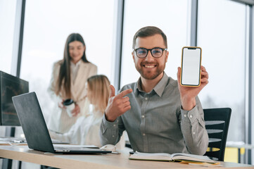 Smiling and holding smartphone. Successful team are working together in the office. Conception of business