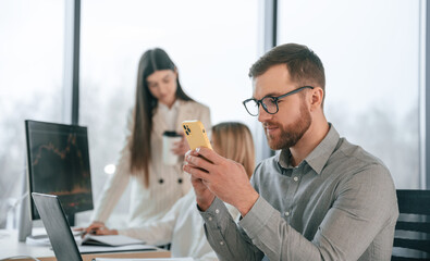 Man is sitting and using smartphone. Successful team are working together in the office. Conception of business