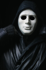 Man in terrible face mask staring at camera against dark background cloak with hood