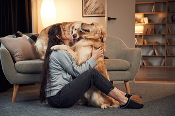 Embracing and having fun. Woman is with two golden retriever dogs at home