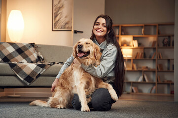 Sitting and smiling. Woman is with golden retriever dog at home