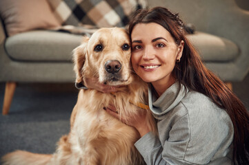 Looking at the camera. Woman is with golden retriever dog at home