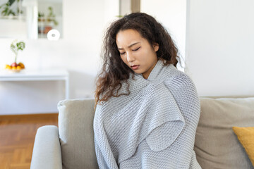 Sick young Asian woman feeling cold covered with blanket sit on bed, ill black girl shivering freezing warming at home wrapped with plaid, no central heating problem, fever temperature flu concept