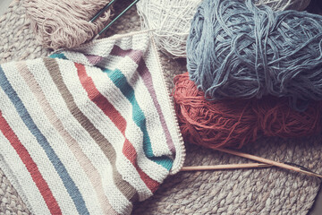 Knitted work in progress. Unfinished striped hat, skeins of cotton yarn and knitting needles.