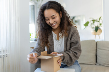 Beautiful young cheerful Asian woman unboxing a package in the living room of a new gift. - obrazy, fototapety, plakaty
