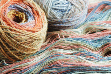 Yarn from natural organic sheep wool. Two balls of multi-colored woolen threads and an unwound skein of rainbow yarn.