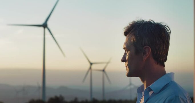 Cinematic close up of engineer putting security helmet on satisfied with his job on background of wind mills with at sunset.Concept: renewable energy,technology,electricity,service,green, future