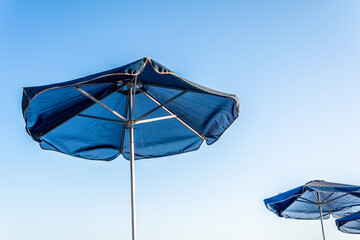 Two blue beach umbrellas with a bright blue sky background on the beach