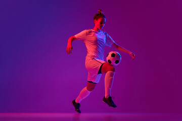 Fototapeta na wymiar Knee kick. Young professional female football, soccer player in motion, training, playing over gradient pink background in neon light