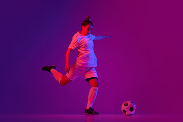 Fototapeta na wymiar Young professional female football, soccer player in motion, training, playing over gradient pink background in neon light. Making goal
