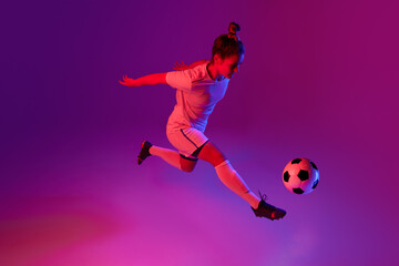 Fototapeta na wymiar Dribbling. Young professional female football, soccer player in motion, training, playing over gradient pink background in neon light
