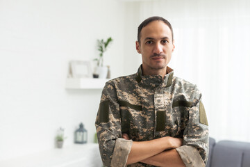 Thoughtful military man staring aside, holding palms by mouth, sitting on couch at home. Young soldier visiting psychologist, suffering from posttraumatic stress, closeup photo, copy space.