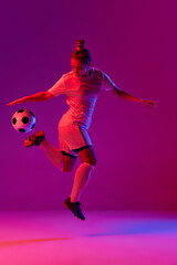 Fototapeta na wymiar Young professional female football, soccer player in motion, training, playing over gradient pink background in neon light. Kick