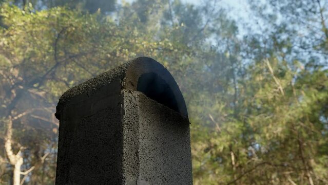black chimney of crematorium works in forest and white smoke comes out of it. concept of end of life and beginning of new one. Smoke rises up wind from stone black pipe in soot.