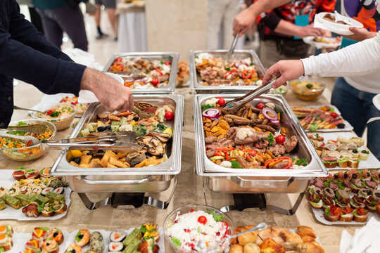Hands picking up food from buffet catering table at the party.