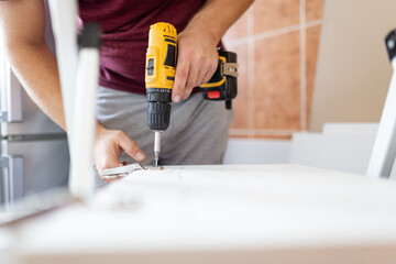 A man assembles furniture, screwing hinges to a wooden door with a screwdriver