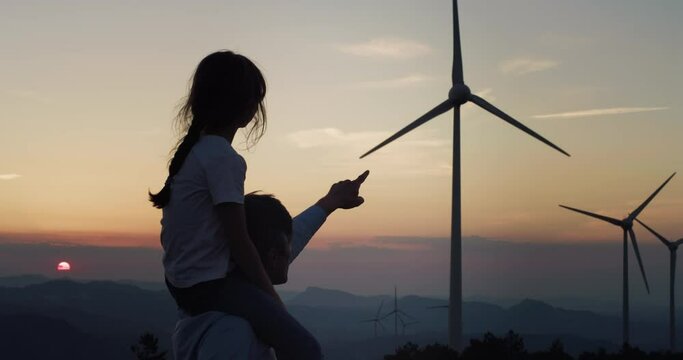 Father and Daughter in a Wind Farm Watching and Pointing at Wind Turbines at Sunset. Aesthetic Shot for Concept of Green Energy and Eco Friendly Environment for Future Generation and our Children