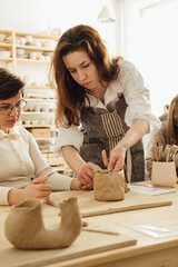 Obraz na płótnie Canvas Portrait of young woman teaching apprentice making ceramics in pottery workshop.