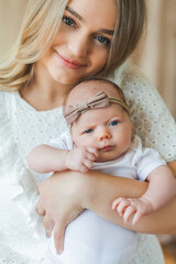 Young beautiful mother with blue eyes holds her little newborn daughter in her arms. Motherhood. Care. Baby.