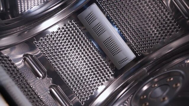 Smooth movement of the chamber from inside the drum of a top-loading washing machine. Shiny surface of perforated stainless steel in household appliances