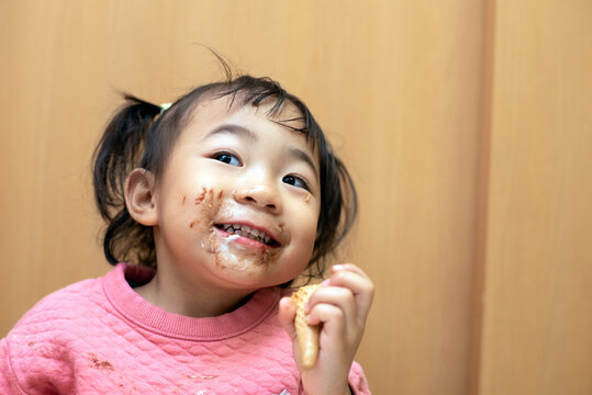 A Happy Toddler Child Eating Chocolate Ice Cream In A Cone With Messy Face