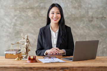 Professional Asian female lawyer or legal advisor sitting at her desk holding hands on books on...