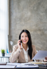 Asian businesswoman sitting on the phone with a customer explaining financial details Earnings and benefits in the office with a happy smile.