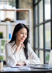 Portrait of a beautiful cheerful Asian businesswoman sitting at her desk with a cup of coffee while taking a break with a happy smile in her upcoming successful business.