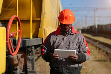 African american railway man with tablet pc at freight train terminal