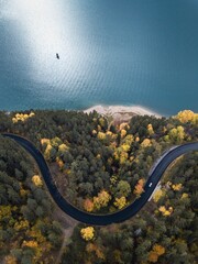 Aerial view of road with car and colorful autumn forest with blue lake in Izvorul Muntelui,Transylvania. Travel or dream concept.