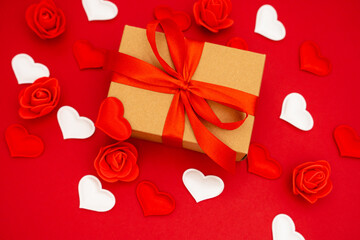 Valentine's Day. Gift box of kraft paper with a red ribbon. Red background with hearts and roses around