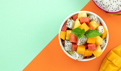 Fruit salad with mango, watermelon, dragon fruit, pineapple, mint on orange-green background. Top view, copy space. Thai fruit salad.