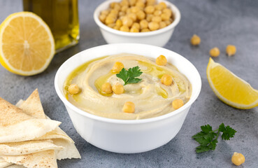 Classic chickpea hummus with pita, olive oil, parsley and lemon on a gray background. Arabic,...