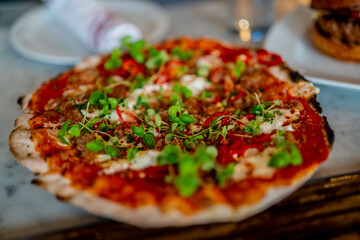 Close up of traditional Italian pizza with green garnish and cheese in restaurant