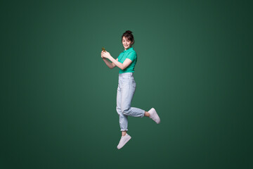Fototapeta na wymiar Full body portrait of young smiling happy woman jump high hold in hand mobile cell phone isolated on green color background. People lifestyle concept