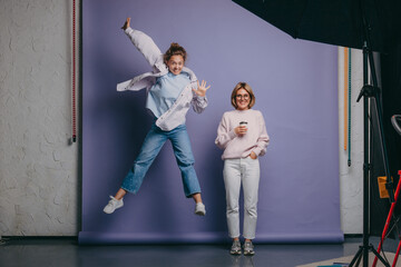 Portrait of two girls standing in the studio and posing in different positions. Happy girls friends together.