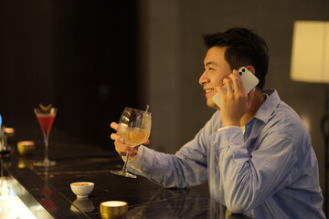 happy cheerful Asian young man on phone call at night bar. side view 