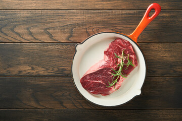 Raw beef steak. Raw fresh Ribeye steak with rosemary, salt and pepper in iron pan on cutting board on dark concrete background. Raw beef steak and spices for cooking.