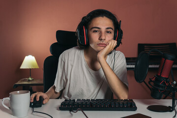 tired or bored streamer using the computer in his bedroom with a microphone and a cup of coffee in the desk