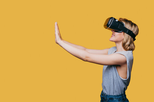 Happy woman getting experience using VR-headset glasses much gesticulating with hands isoalted over yellow background. Free space for text. Copy space.