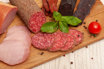 Different types of sausages ham, mahan, salami on a wooden board decorated with tomatoes and basil