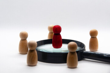 Red wooden doll on top of magnifying glass surrounded with other wooden figure. Leadership and teamwork concept