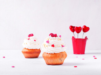 Cupcakes topped with whipped cream, heart shaped sprinkles and raspberry on white table. Dessert for Valentine Day or wedding