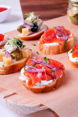Bruschetta assortment with salted trout, red onion, cream cheese, red caviar, pickled cheese, and microgreens served on wooden board. Set of appetizers with various toppings
