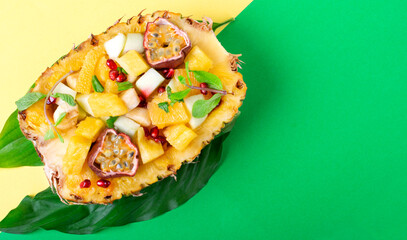 Obraz na płótnie Canvas Fruit salad served inside pineapple half. Orange, apple, banana, pineapple, pomegranate and passion fruit chopped and mixed in the natural bowl